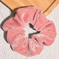 Detail van een roze fluwelen haarscrunchie met zachte glans op een houten dienblad - Roze