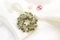 Elegant gold metal wreath brooch with green crystal stones on beige silk fabric - Green
