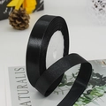 Glossy black satin ribbon roll on a lifestyle background with yellow gift boxes - Black
