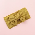 Close-up of mustard yellow ribbed fabric baby headband with large bow on pink background - Ginger Yellow