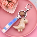 Détail d'un porte-clés dinosaure avec l'attache en métal et la dragonne holographique rose - Style avec Dragonne et Perle / Marron