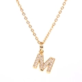 Macro detail of gold-plated letter M pendant with paved white zircons on a cable chain - Letter M