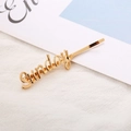 Detail view of a golden alloy hair clip featuring Sunday script lettering on fabric - Sunday