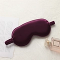 Deep purple satin sleep mask with elastic strap shown on a textured white surface - Deep purple