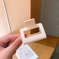 Close-up of a matte cream rectangular hair claw clip held in hand with wooden background - Beige