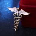 Dettaglio della spilla caduceo dorata con ali in smalto bianco su velluto rosso - Oro Antico