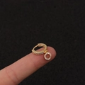 Nahaufnahme kleiner goldener Blitz-Ohrringe mit Zirkonia-Steinen auf einer Fingerspitze - Silber / Rund