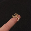 Nahaufnahme einer goldenen Creole mit Blitzanhänger und Kristallen auf der Fingerspitze - Silber / Mond