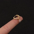 Nahaufnahme einer goldenen Creole mit funkelndem Zirkonia-Blumenanhänger am Finger getragen - Silber / Blume