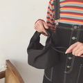 Minimalist black baguette bag with pleated fabric texture held by a model on white background - Black