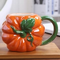 Glossy orange pumpkin ceramic mug with a green leaf handle on a wooden coaster - Orange