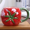 Detail of red tomato-shaped ceramic mug with green leaf handle on a warm home background - Tomato Shape / Watermelon red