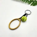 Dettaglio ravvicinato di mini racchetta da tennis e portachiavi a pallina verde soffice - Oro