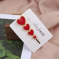 Gros plan d'une barrette dorée avec quatre cœurs en émail rouge sur carte de support - Rouge