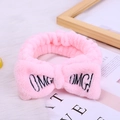 Pink coral fleece head band with OMG! embroidery bow on white plush surface - Pink