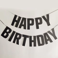 Glittery black Happy Birthday banner hanging against a white wall for party decor - Black Glitter Birthday