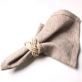 Detail of a natural jute woven napkin ring on a beige linen fabric with rustic texture - Natural Hemp Rope