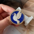 Macro detail of peace dove enamel brooch with a textured gold border and olive branch - White Dove Blue