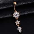 Gold belly ring with floral and teardrop crystal pendants on a textured black surface - Gold