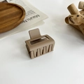 Vista macro dettagliata di una pinza per capelli marrone chiaro opaco su sfondo in legno - Piccolo cubo / Caffè chiaro