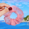 Pink checkered organza hair scrunchie with daisy pattern held against a beach background - Pink Plaid