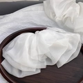 Detail of multi-layered white chiffon bow hair clip with translucent organza on wood tray - White