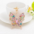 Golden butterfly keychain with colorful rhinestones placed near a white tea cup - Colorful