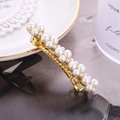 Primer plano de un clip para el cabello dorado con perlas blancas en un plato - Perla Completa
