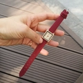 Detaillierte Nahaufnahme einer quadratischen roségoldenen Uhr mit weinrotem Lederband - Rot