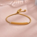 Close-up of adjustable gold box chain bracelet with smooth curved plaque and bead charm - Kids / Gold