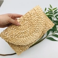 Handmade woven straw clutch bag in beige with semicircular flap held by hand - Light Coffee