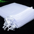 Detail of white organza gift bags showing transparent mesh texture and drawstring closure - 7x9cm