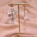 Details von asymmetrischen Barockperlenohrringen mit Goldblüten auf Seidenstoff - Asymmetrische Blumen-Hängeohrringe