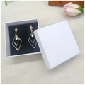 Detail of gold geometric earrings with black gems in a white square gift box with a rose - White