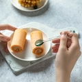Mano che tiene un cucchiaio di vetro resistente al calore su rotoli di torta dorati - Verde Scuro