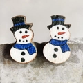 Macro view of handmade wooden snowman earrings with festive blue scarf and black hat - Snowman