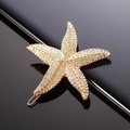 Golden starfish metal hair clip with a textured finish shown on a reflective black base - Metallic Gold Starfish