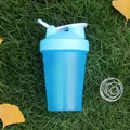 Close-up of blue fitness shaker bottle with a stainless steel whisk ball on grass - Blue