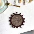 Set de table rond tressé marron et beige avec petits pompons sur surface blanche - 13cm Dessous de verre / café