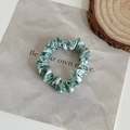 Dettaglio di uno scrunchie in seta mimetica verde su sfondo marmoreo con decoro in legno - Pied-de-poule Verde