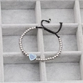 Detalle de la pulsera tejida con cuentas y dije de corazón con circonitas azules - Oro Blanco