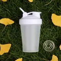 Detail of portable shaker bottle with whisk ball on autumn grass for protein shakes - White