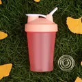 Close-up of portable red shaker bottle with mixing ball on grass with autumn leaves - Red