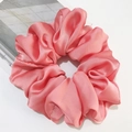 Oversized peach satin scrunchie with soft ruffled pleats shown against a magazine backdrop - Peach Pink