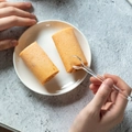 Rotoli di pan di spagna arancioni con ripieno di crema su piatto bianco e cucchiaio - Trasparente