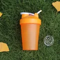 Close-up of orange fitness shaker bottle with mixing ball on green grass and autumn leaves - Orange