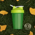 Detail of green sports protein shaker bottle with stainless steel mixing ball on grass - Green