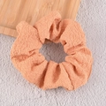 Détail de la texture du chouchou en seersucker abricot sur fond minimaliste - Orange