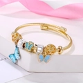 Golden spiral bracelet with pink and blue butterfly charms on a white display stand - Blue Butterfly