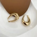 Vue détaillée de boucles d'oreilles créoles ovales épaisses dorées sur un plateau blanc - Doré